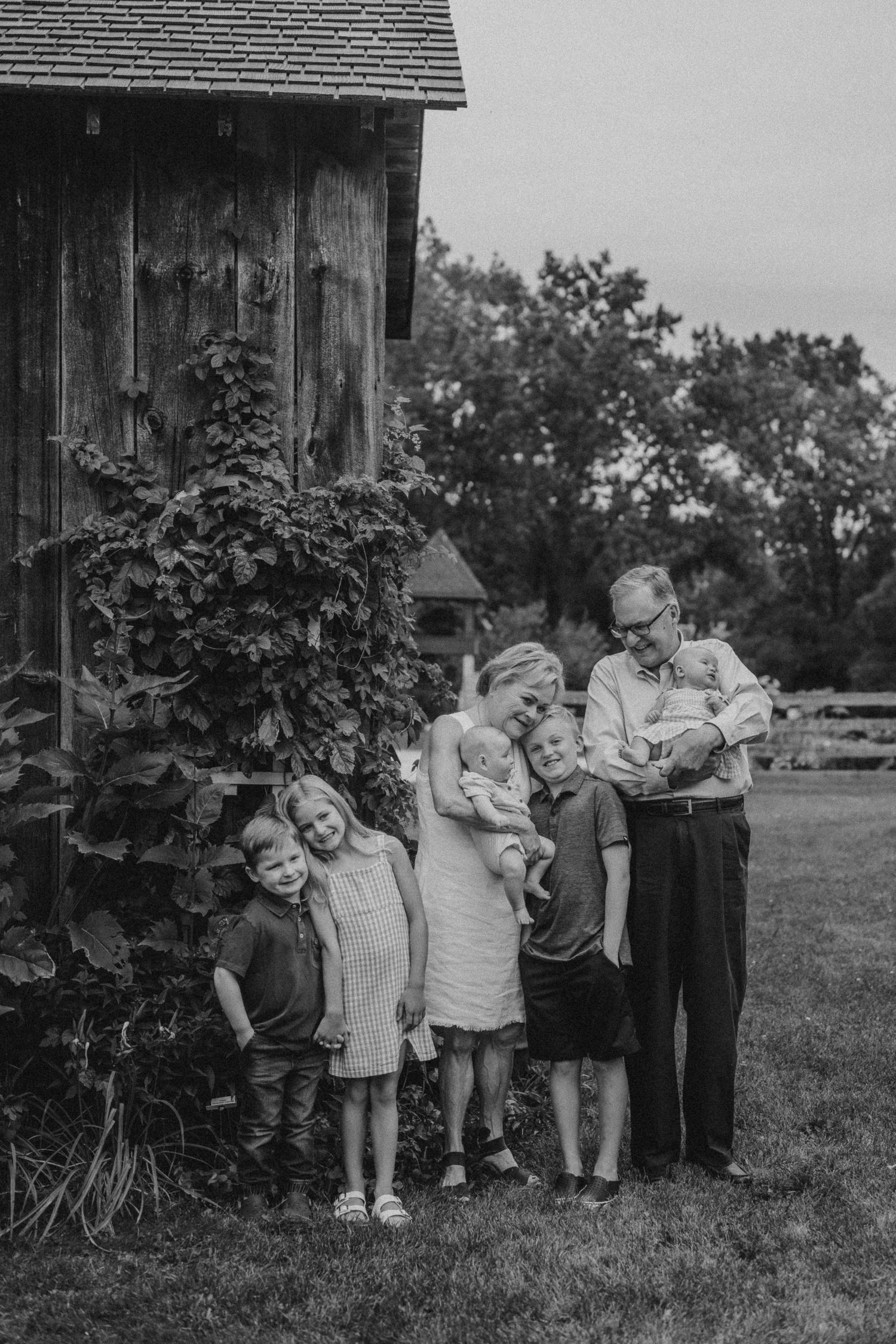 Vintage black and white photograph of group standing beside rustic wooden building with climbing vines.