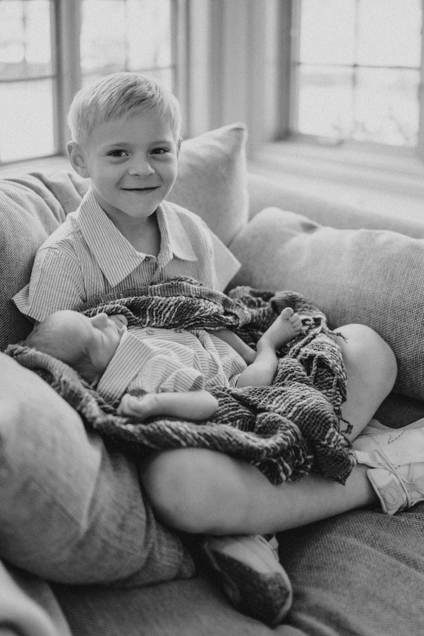 Black and white photo showing tender moment between siblings on couch with blanket.