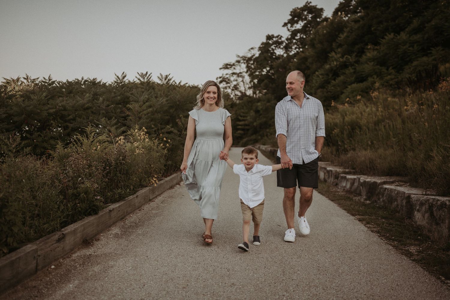 A family of three walks together on a paved path during golden hour.