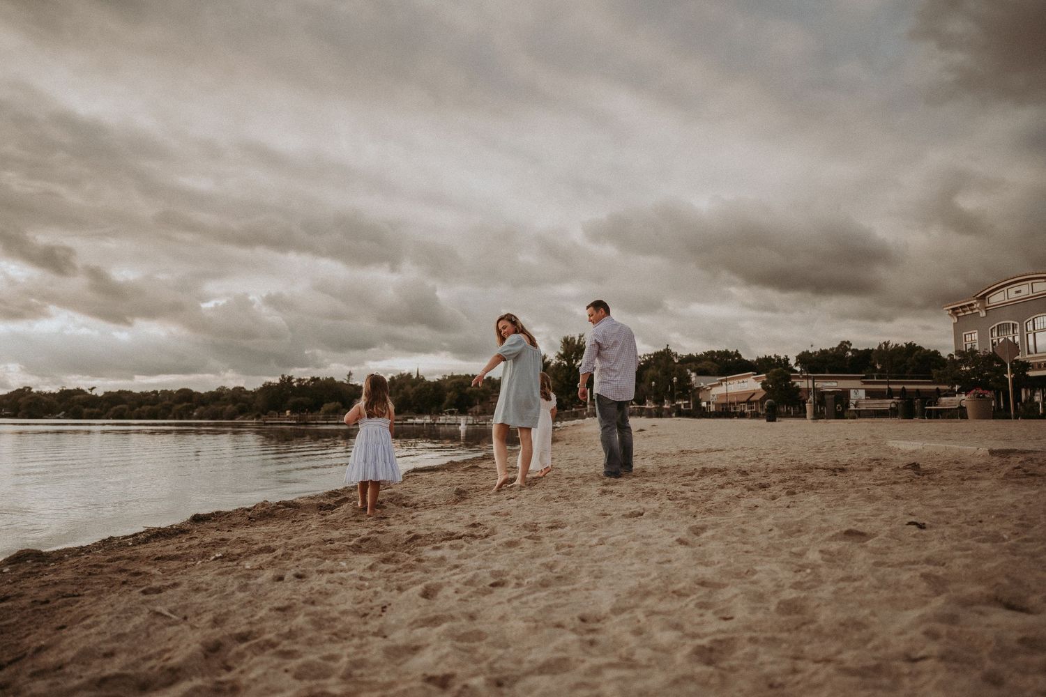 Family walks together along a sandy beach shoreline under moody evening skies.