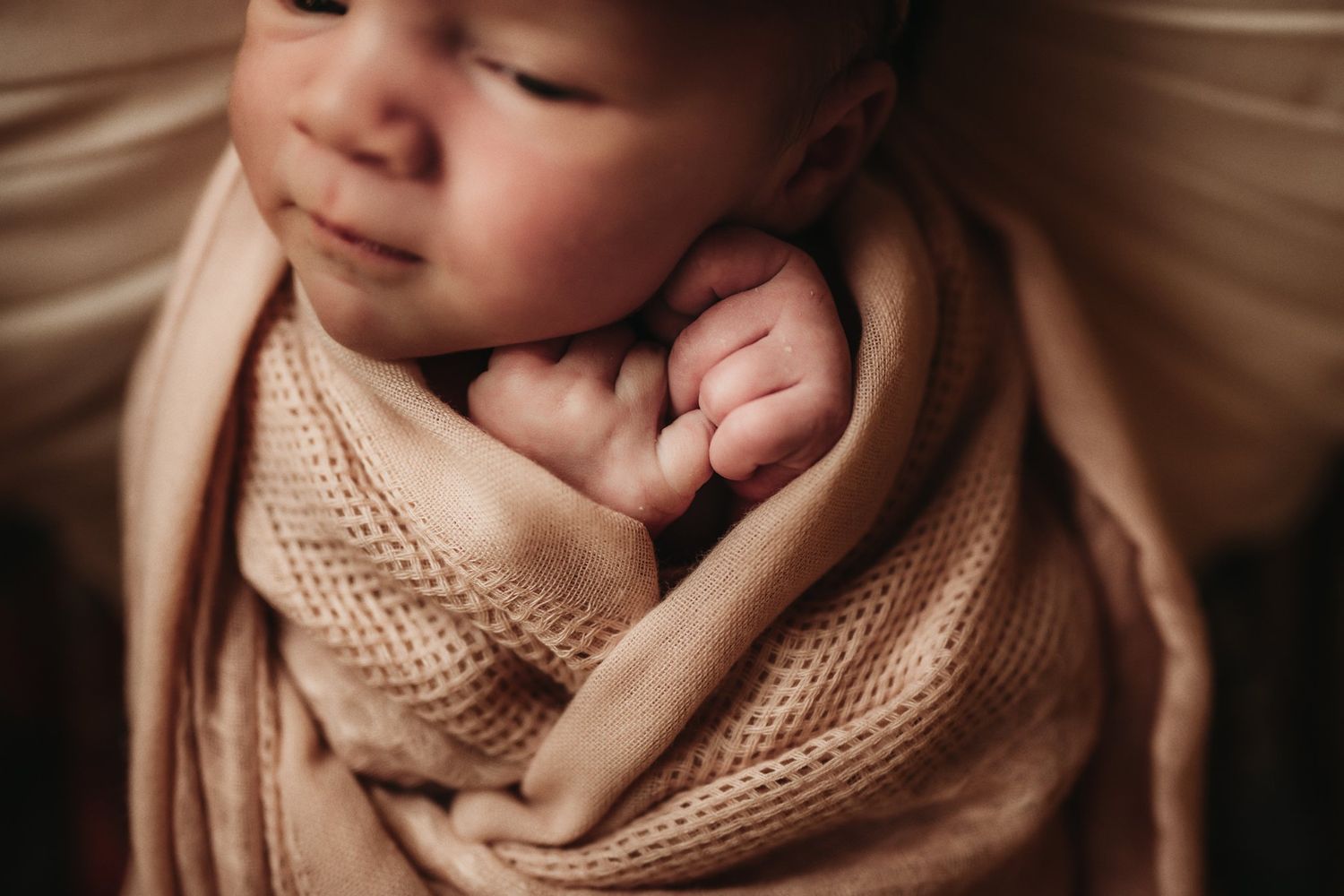 Close-up of peaceful sleeping newborn wrapped in knitted beige blanket.