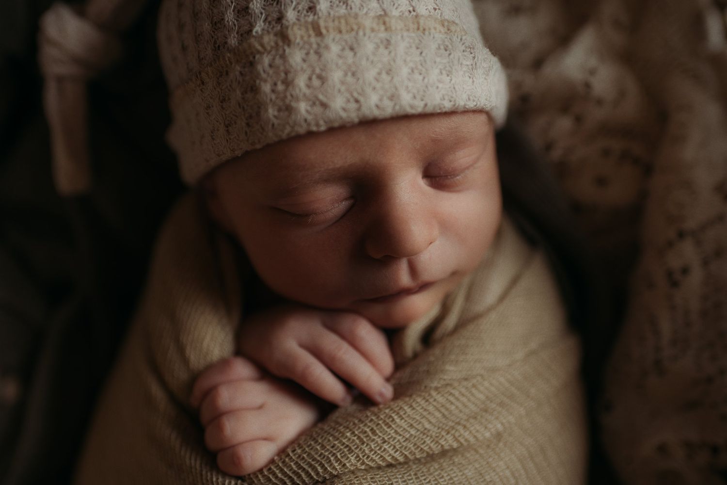 Peaceful sleeping newborn wearing knit hat and wrapped in soft neutral swaddle.