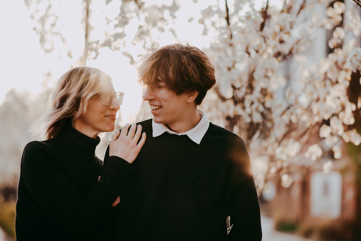 Intimate portrait of couple in black clothing with blossoming trees in background.