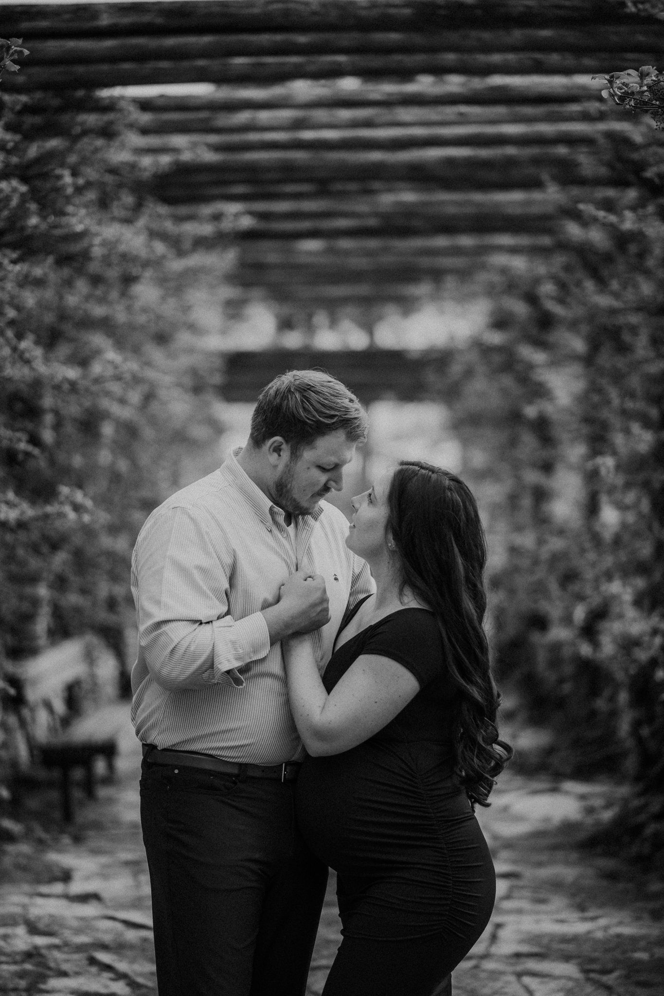 Romantic black and white maternity photo under a rustic pergola.