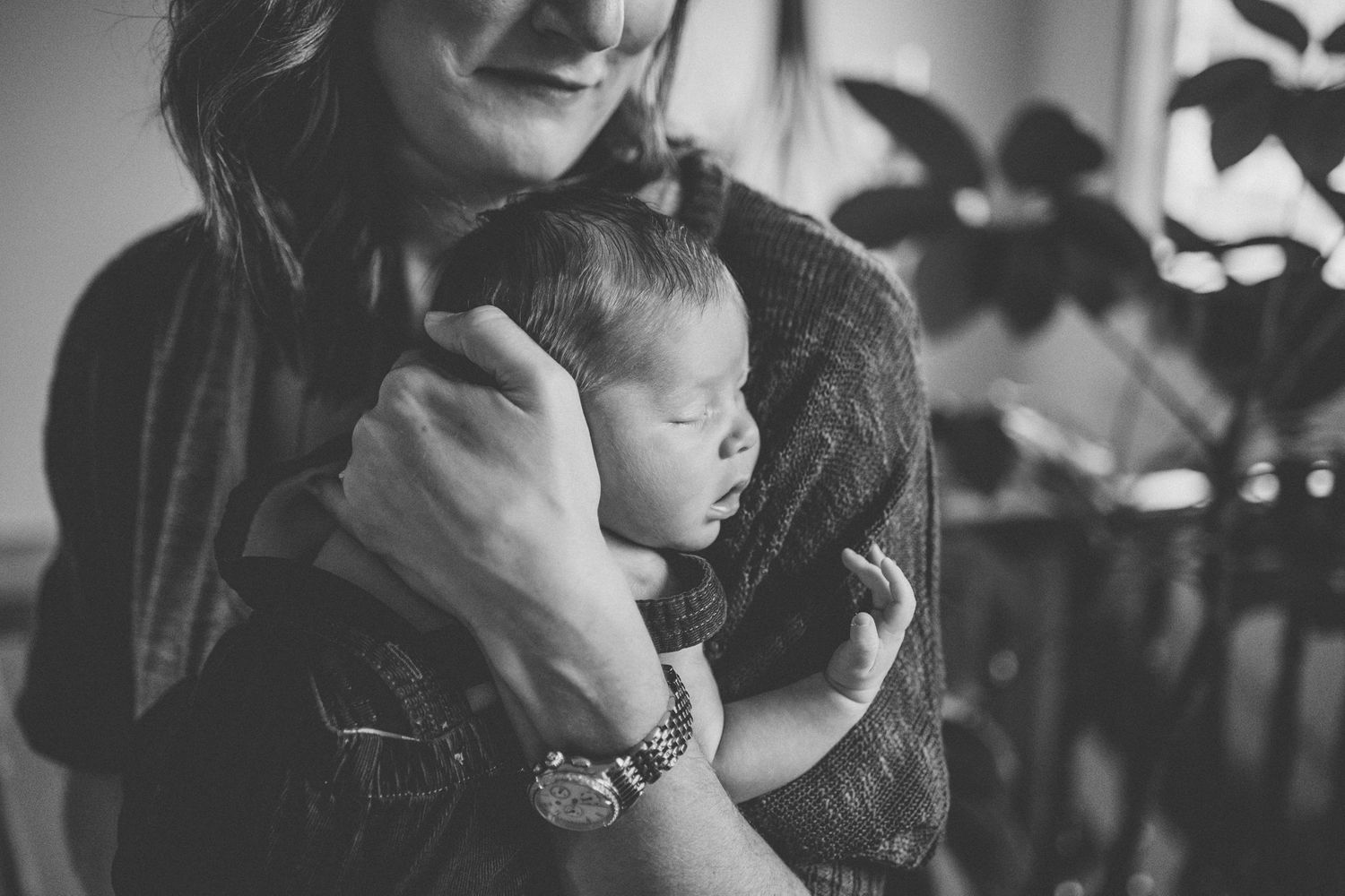 Black and white portrait capturing tender moment between adult and sleeping infant.