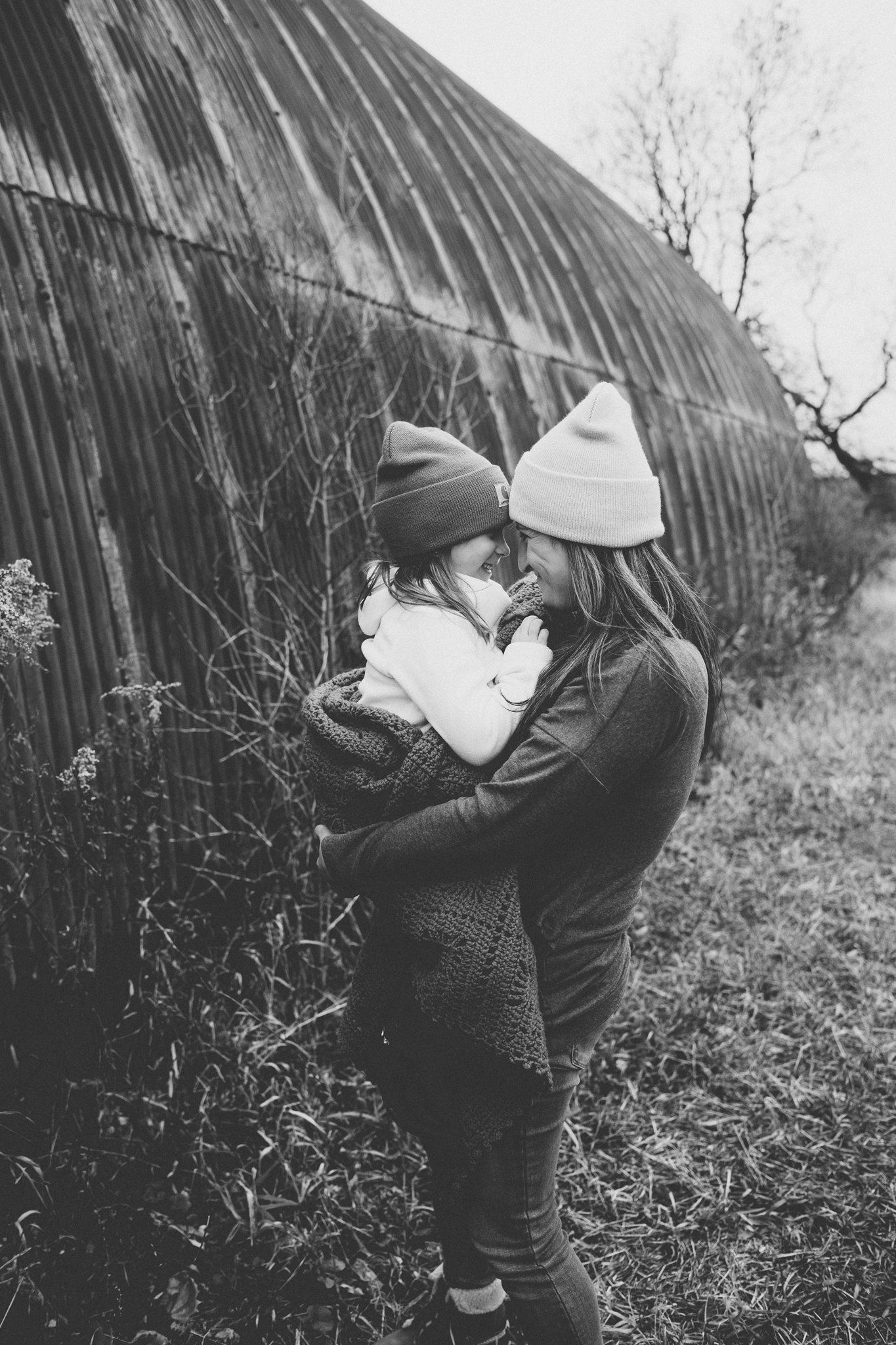 Black and white portrait against rustic curved barn wall during a winter family photo session.