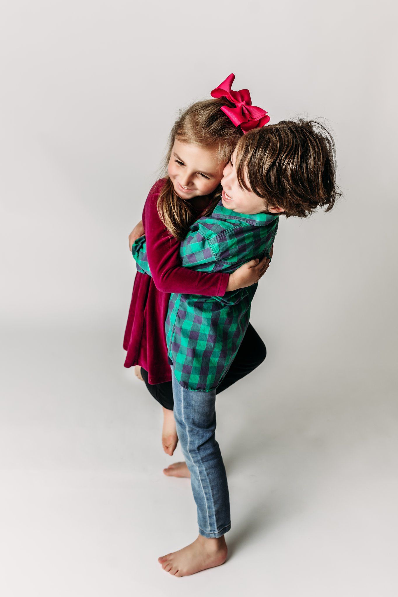 Two children hugging and laughing together against white background.