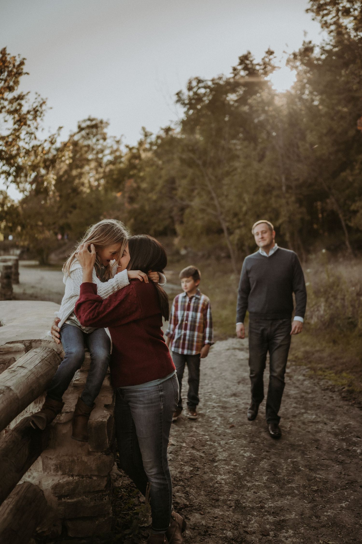 A candid family moment captured along a rustic wooden fence trail during golden hour.