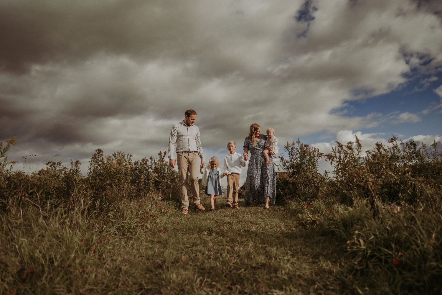 A family walks together on a hilltop path under dramatic cloudy skies.
