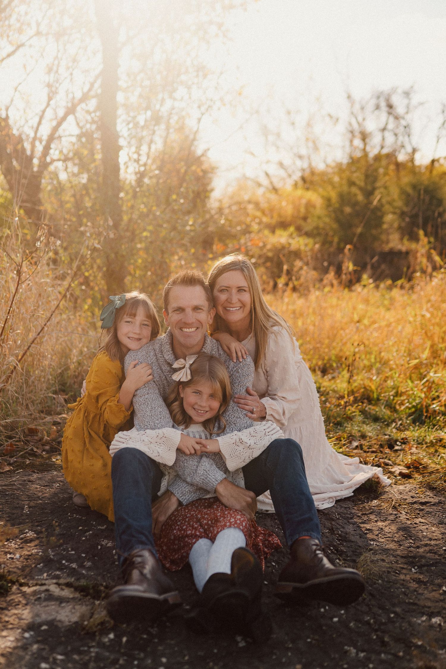 A family of four sitting together outdoors during golden hour in autumn scenery.