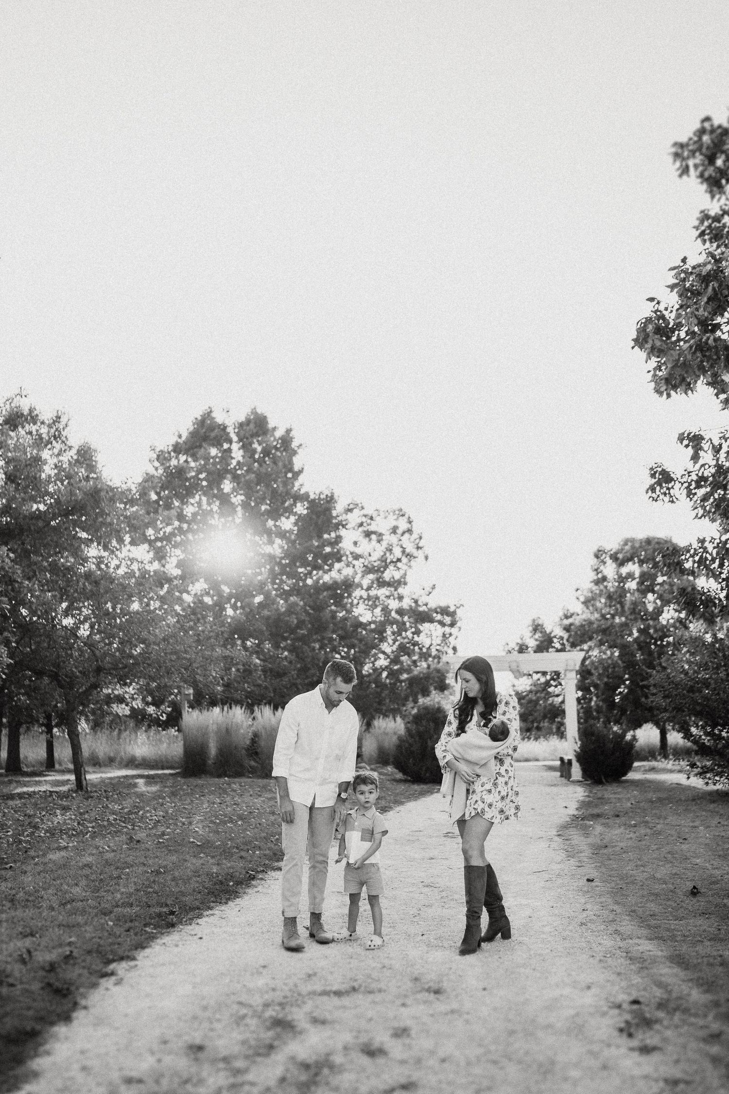 Black and white photo of family walking together on tree-lined path.