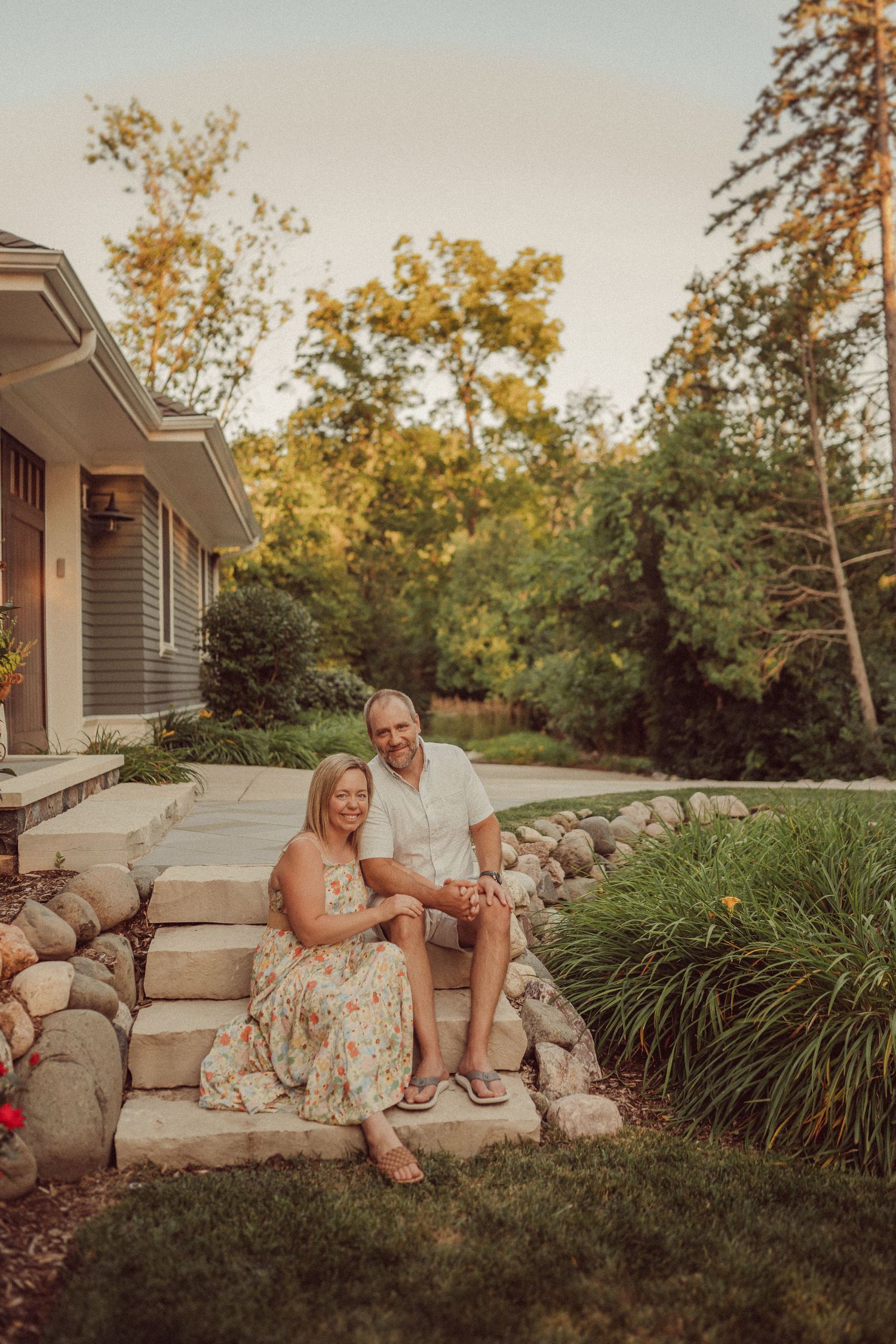 Couple sitting on rock steps in front of a house during golden hour.