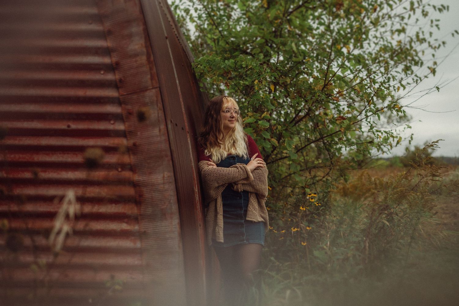 Artistic portrait through branches against weathered red metal structure.