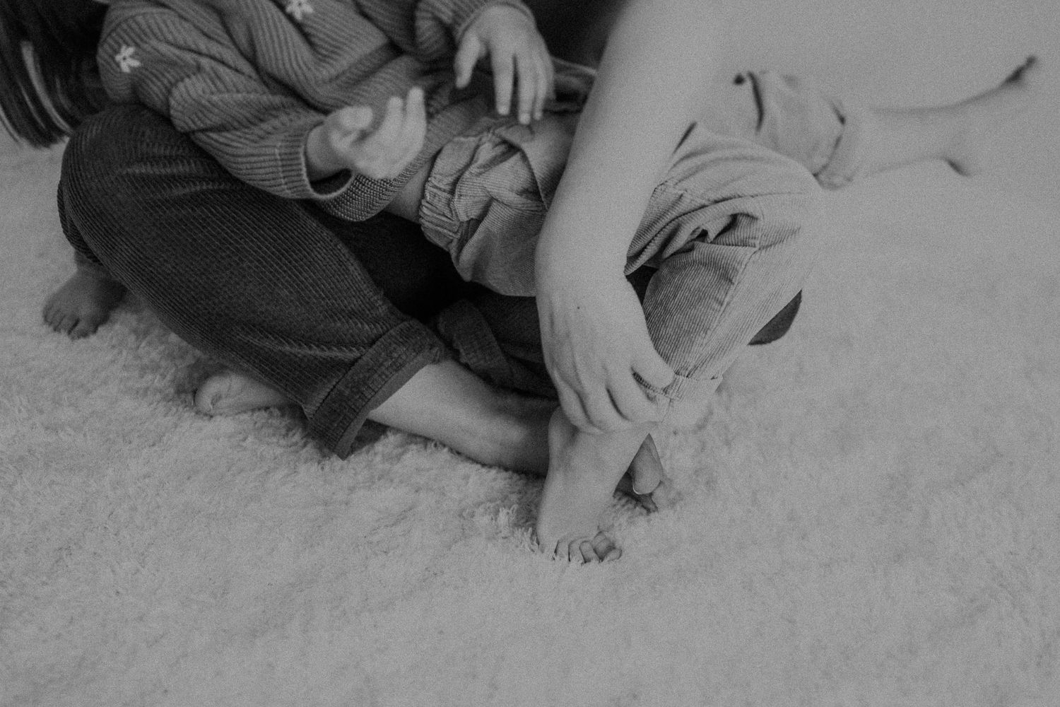 Two people's feet and legs on a light carpeted floor in black and white.