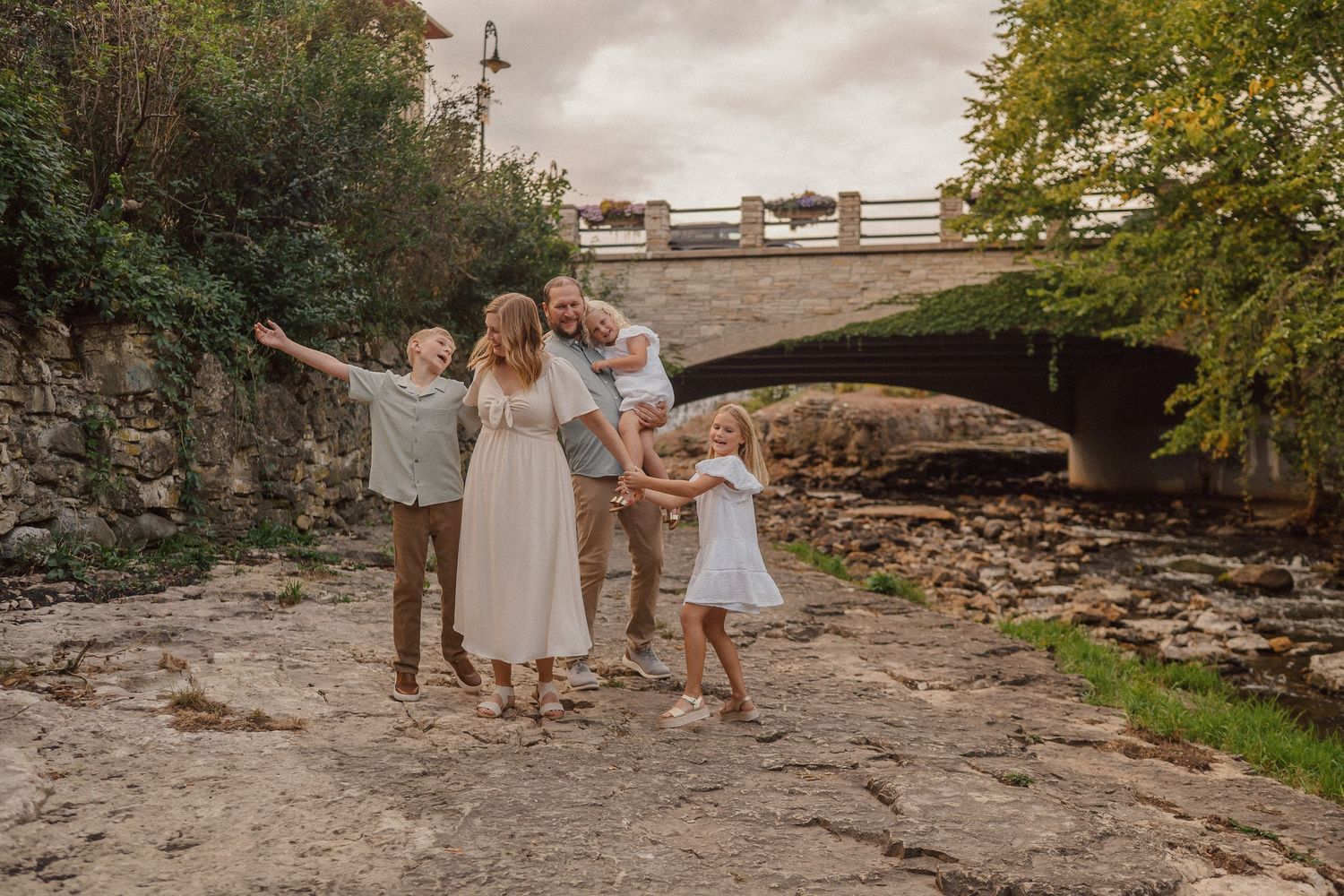 Family members play and interact on rocky terrain surrounded by natural stone walls and greenery.