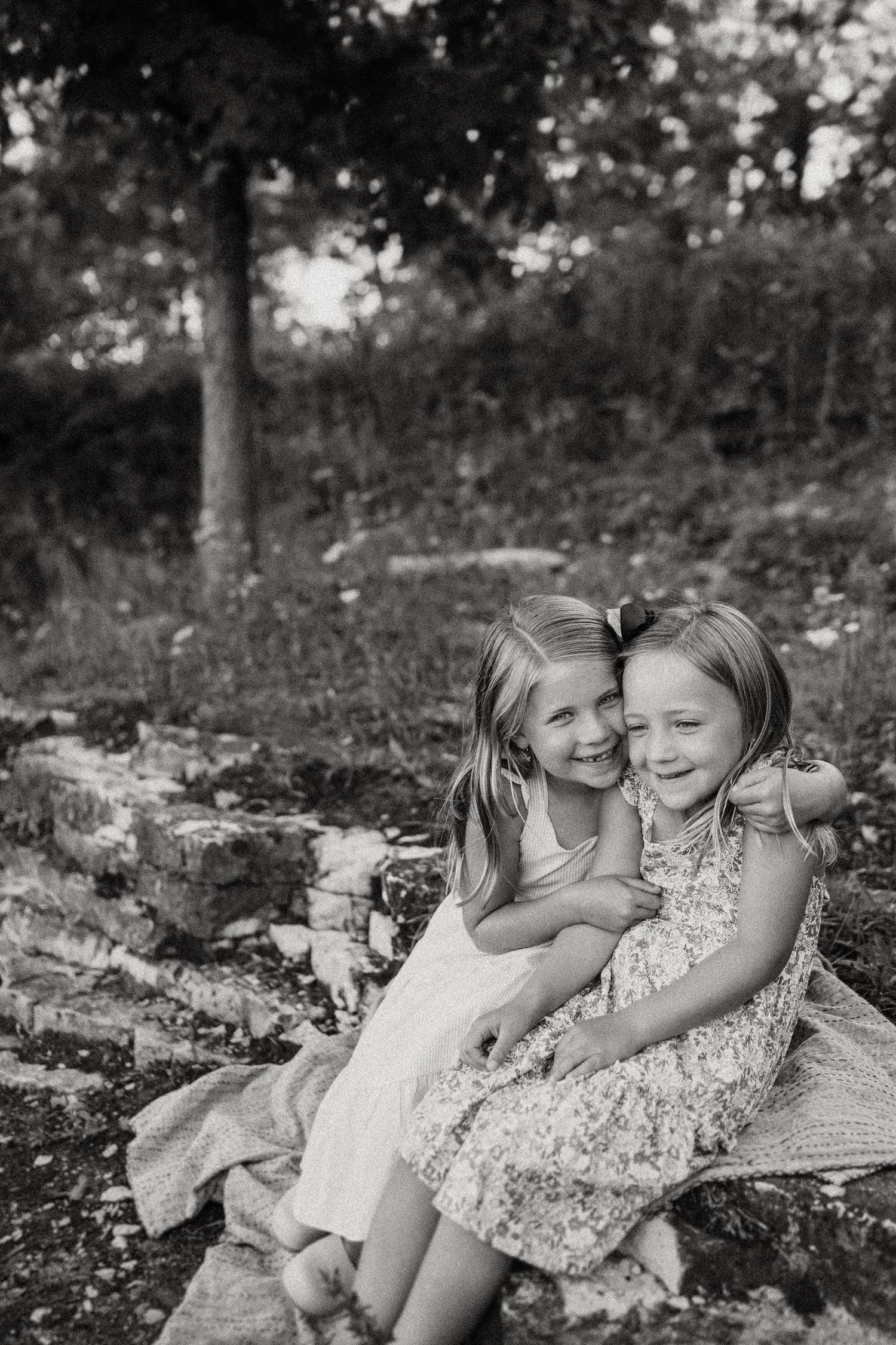 A black and white capture of two children sharing a candid moment on rocky terrain.