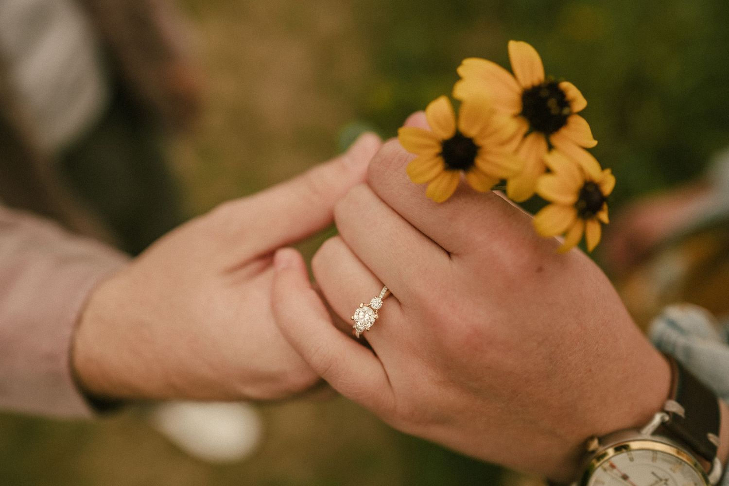Close-up of hands holding yellow wildflowers with engagement ring visible.