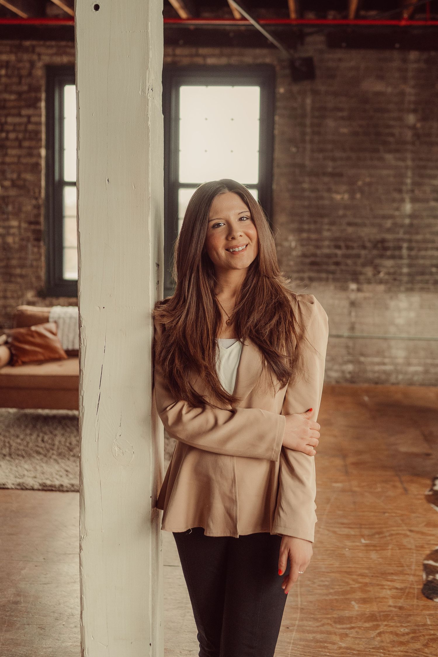 Lifestyle portrait next to white column featuring beige blazer in industrial space.