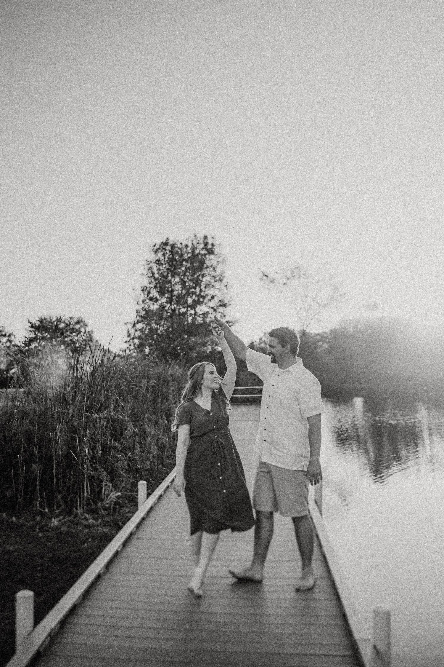 Black and white photo of two people strolling on a lakeside boardwalk at dusk.