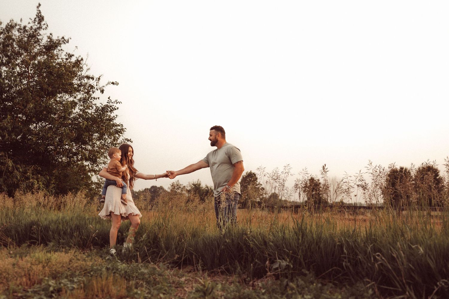 A couple holds hands while standing apart in a golden summer field.