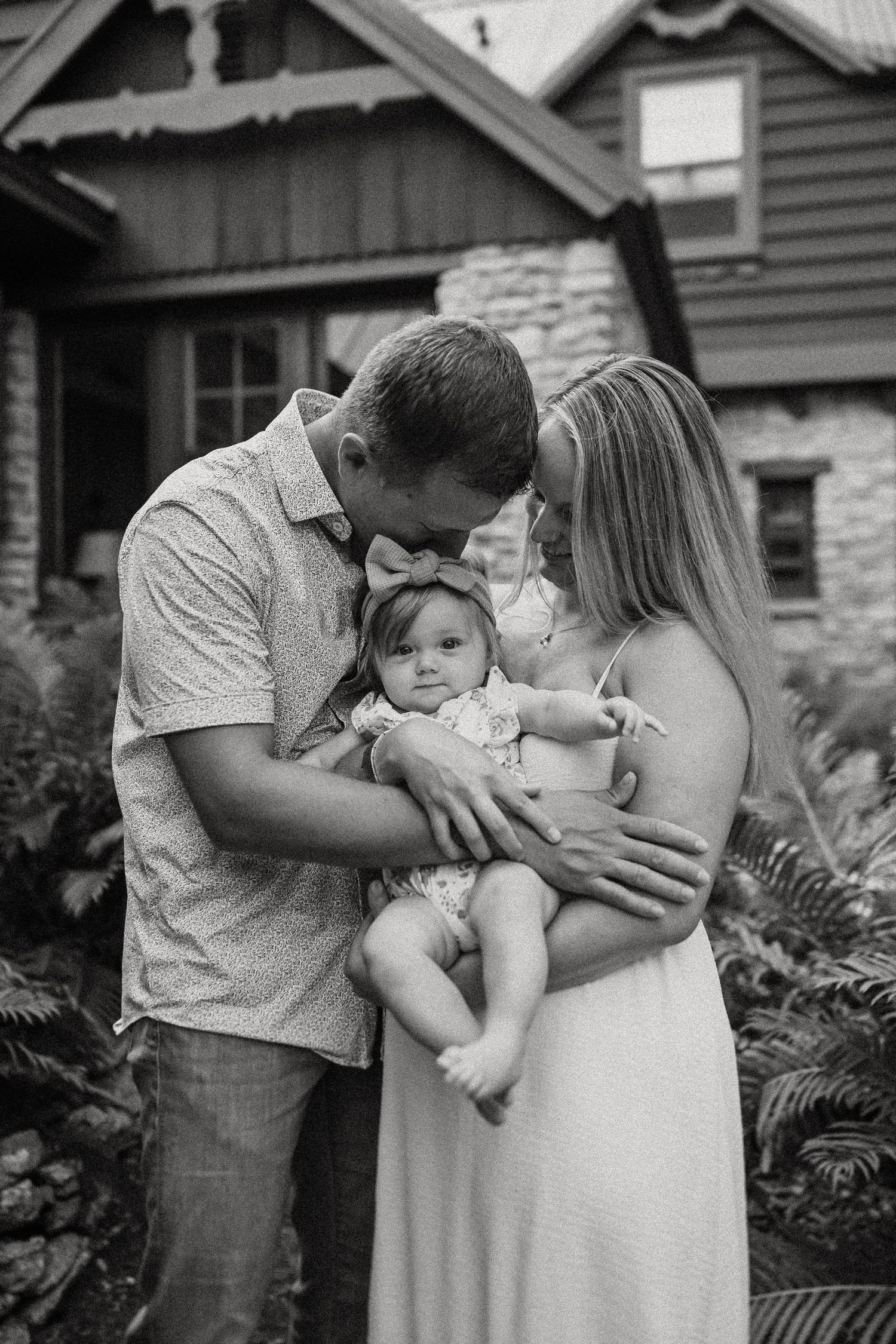 A tender family moment outside a stone cottage with lush ferns in the foreground.