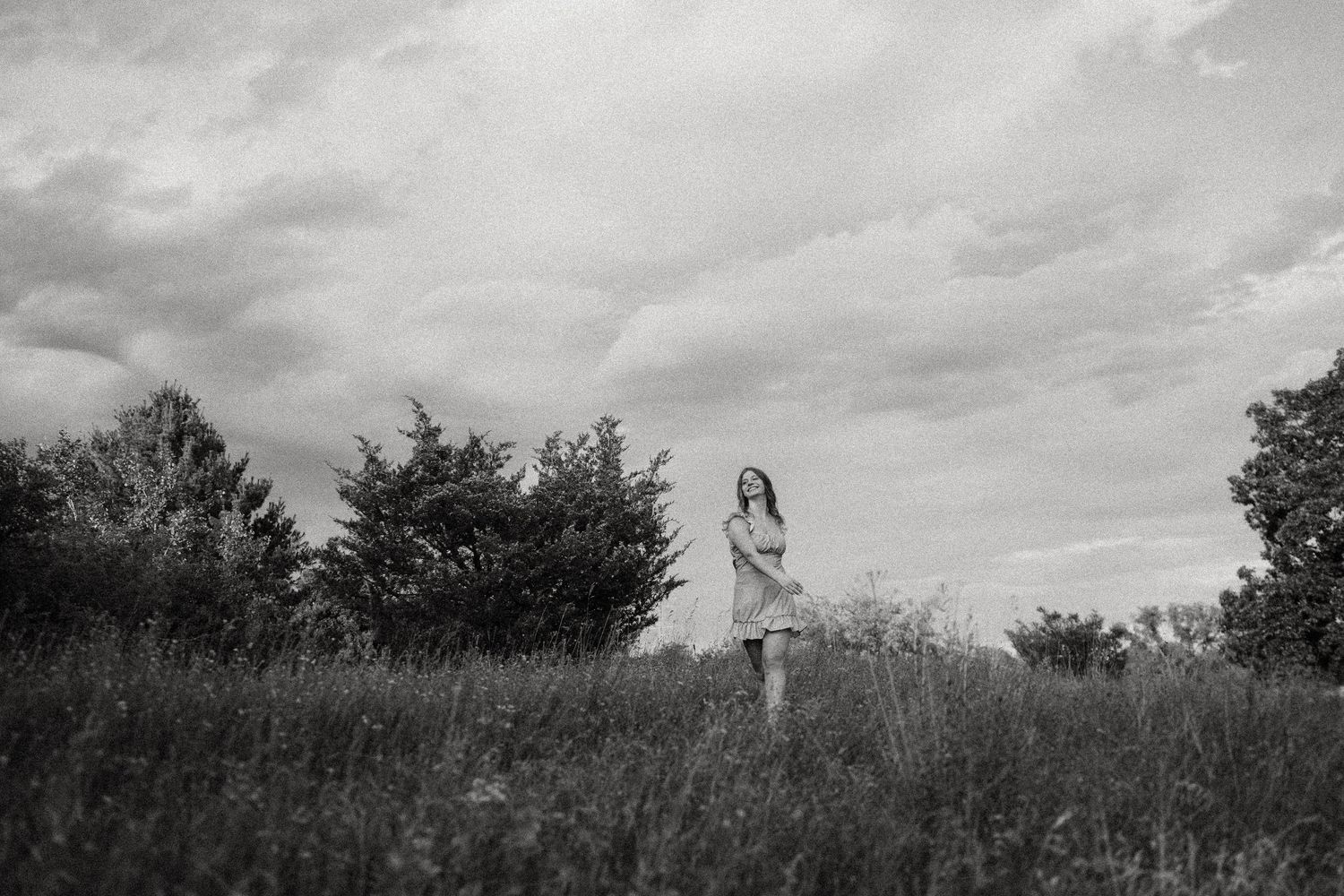 Monochrome silhouette of person standing alone on hilltop with moody cloud formations.