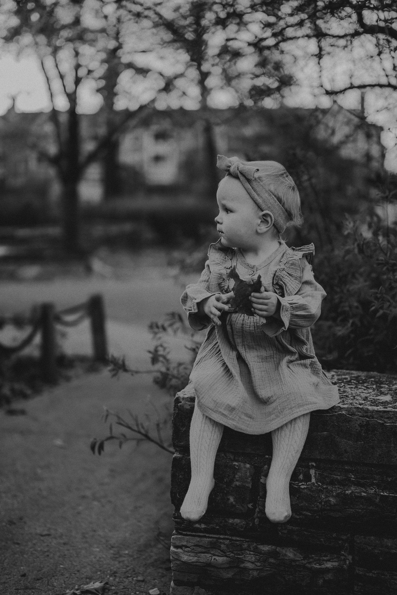 Vintage black and white photo of small child sitting on wooden fence.