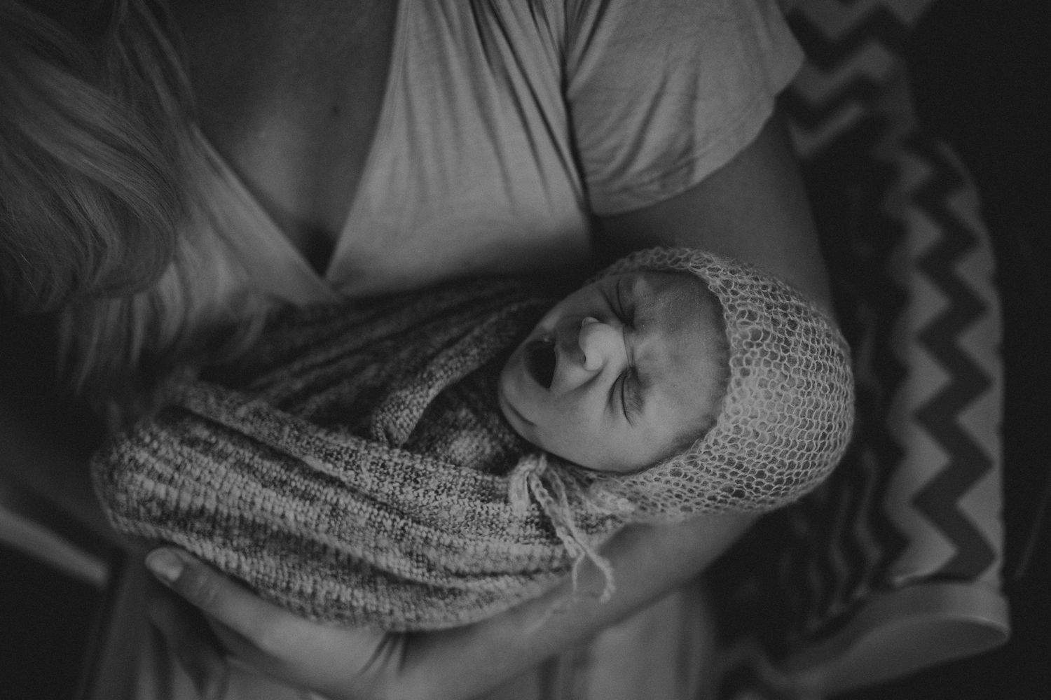 Black and white portrait of sleeping baby wrapped in knitted blanket.