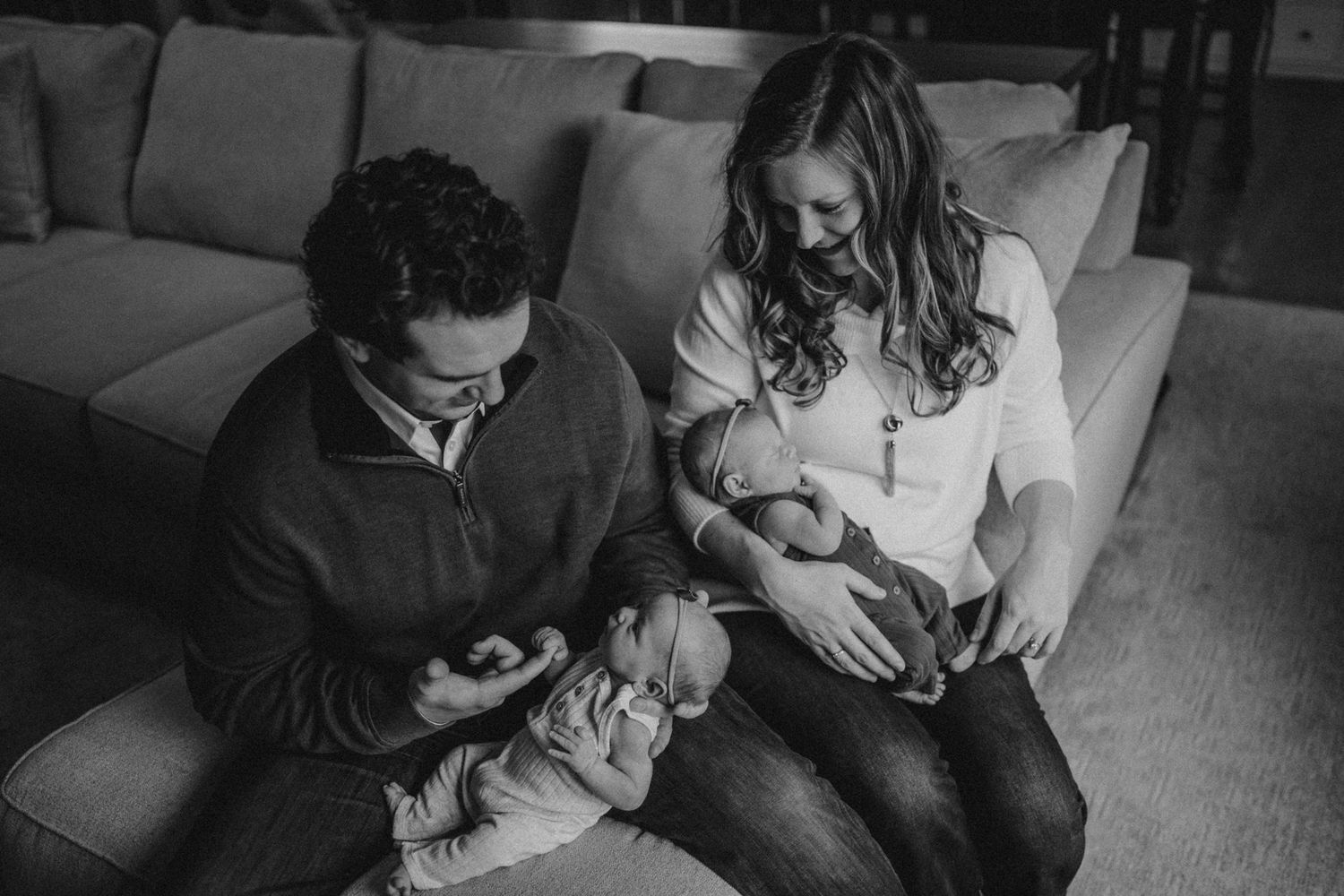 A black and white photo of parents sitting on a couch with their newborn baby.