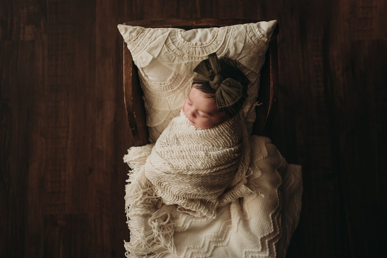 Overhead view of sleeping baby wrapped in cream textiles on soft pillow.