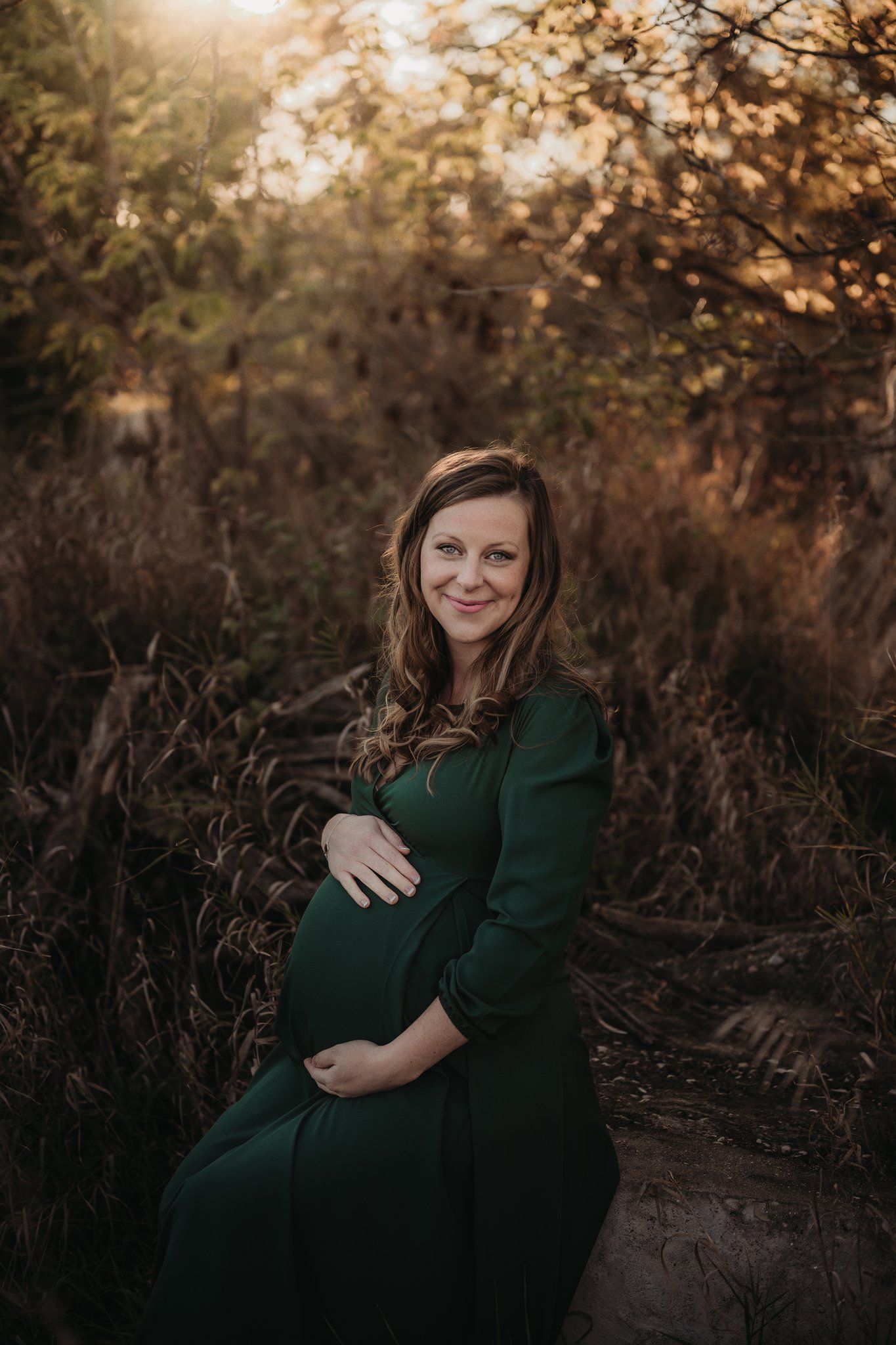 Expectant mother in green dress poses during golden hour maternity shoot.