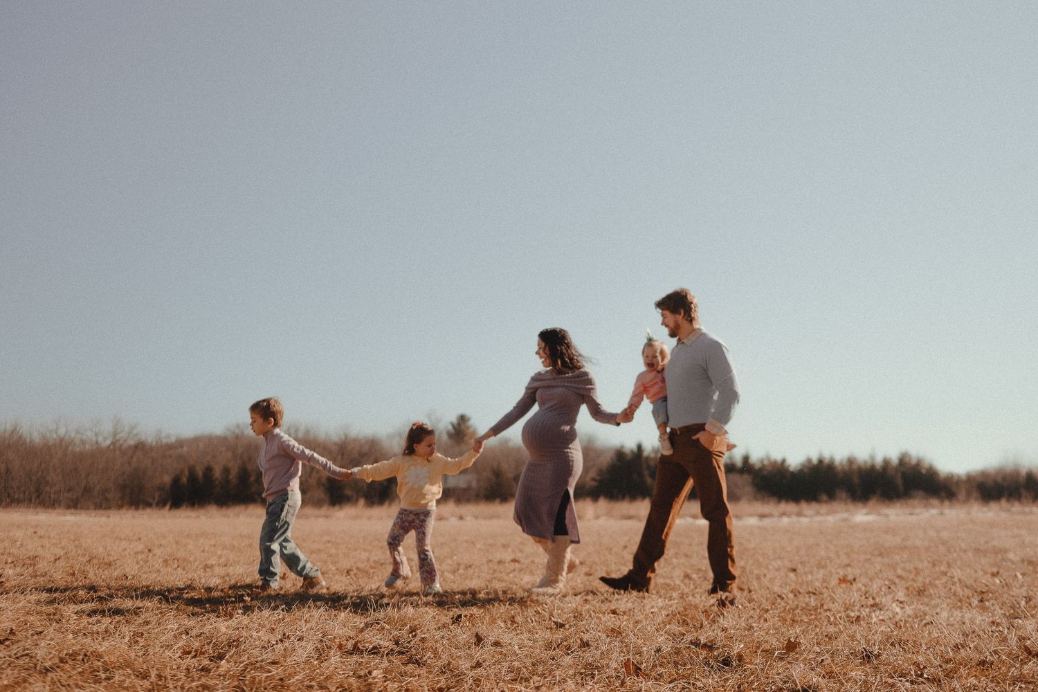 A series of photos showing people playing and falling together on a grassy field at sunset.