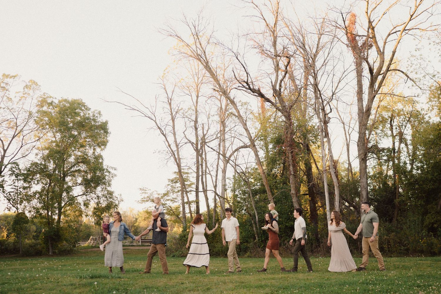 Group walking through a field at sunset with bare trees in the background.