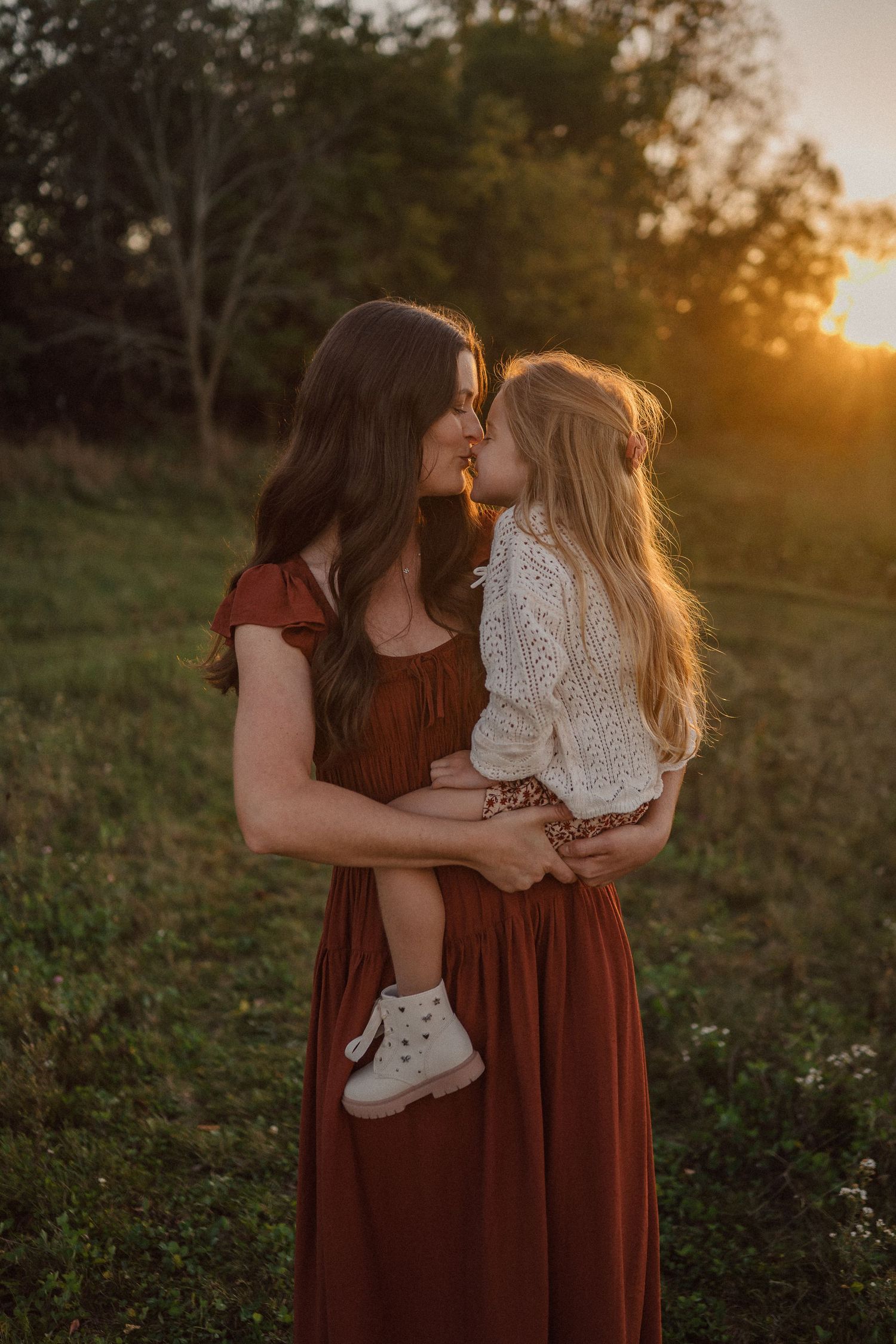 Two people in burgundy dresses share an intimate moment in golden evening light.