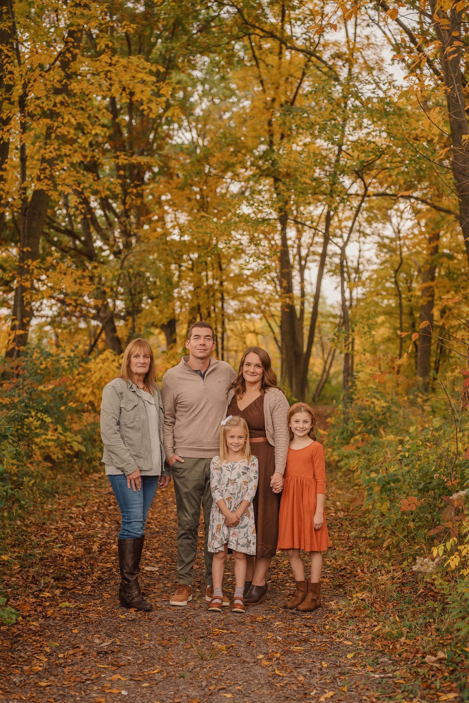 A group poses together on a wooded trail surrounded by golden autumn foliage.