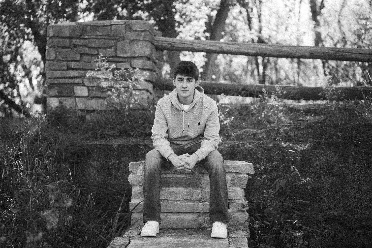 A person sits on a stone wall in a contemplative pose while looking down at the ground.