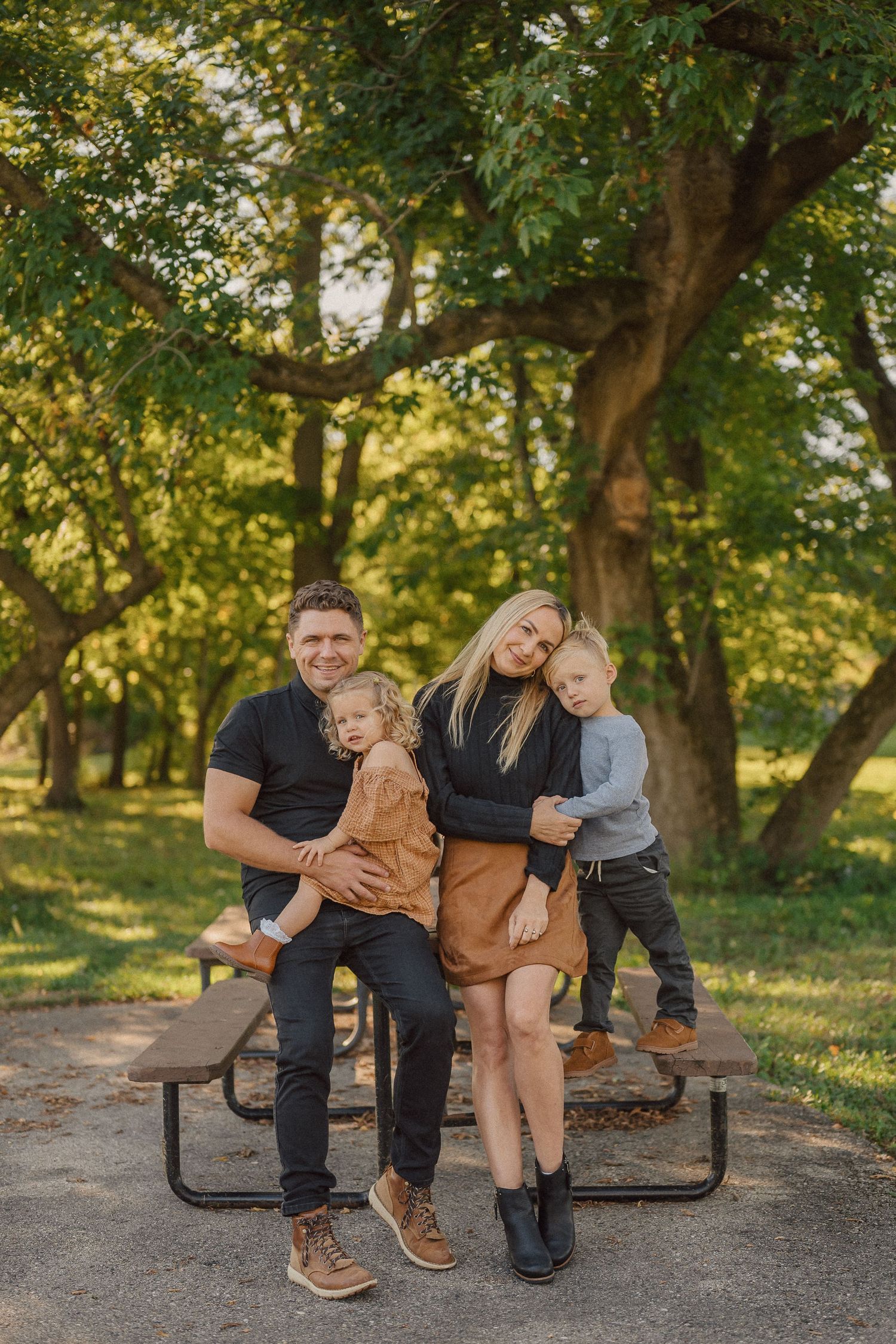 A family relaxes together on a wooden bench in a sunlit park during autumn.