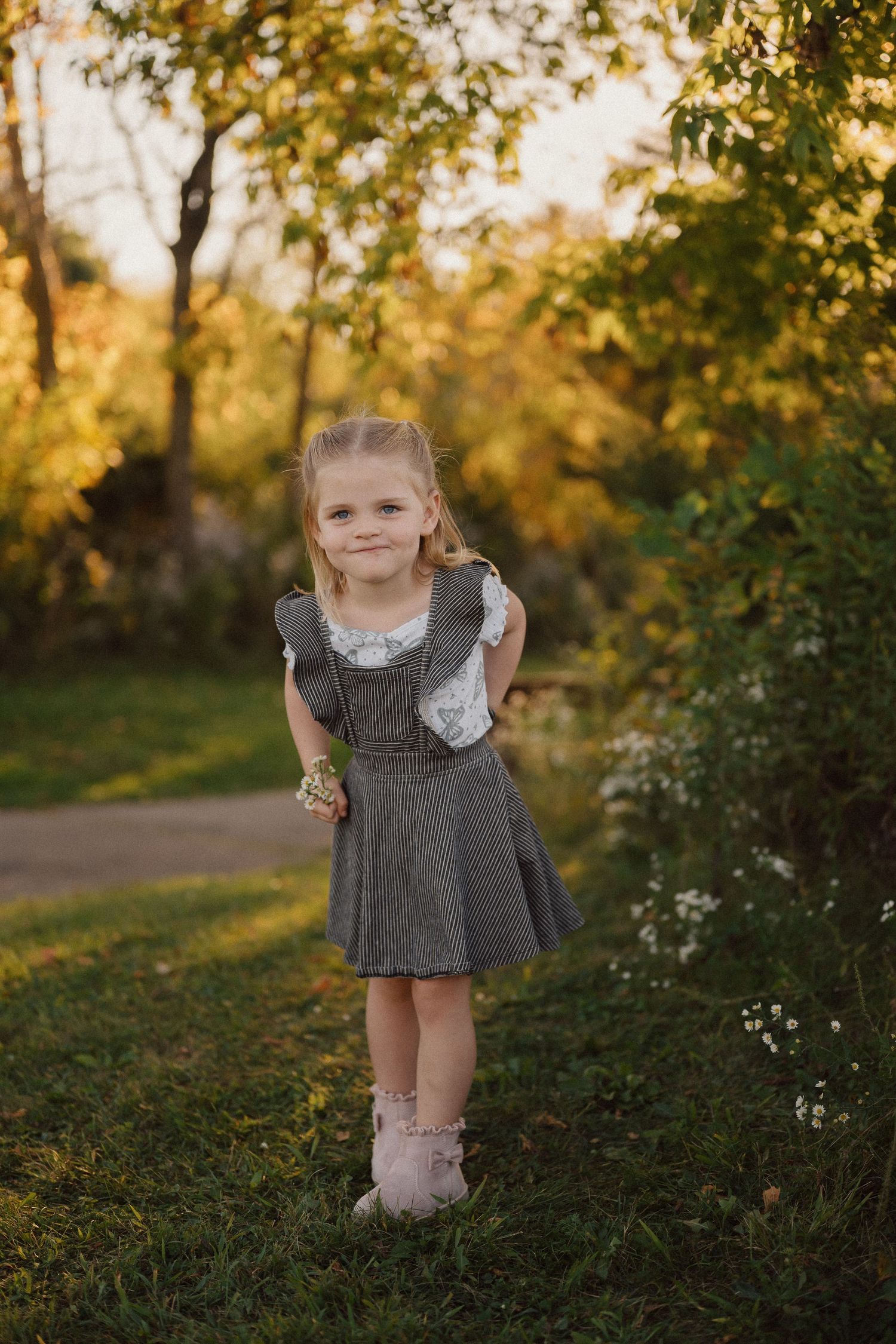 Young child in gray dress playing in field during golden hour sunset.