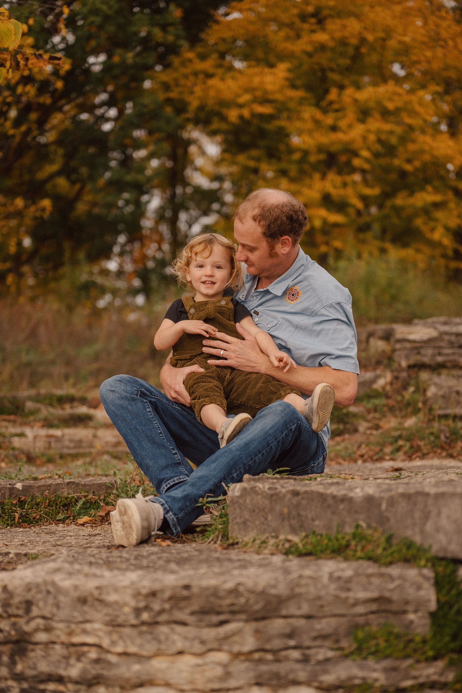 Sweet playful interactions unfold on a stone ledge against a backdrop of golden fall trees.