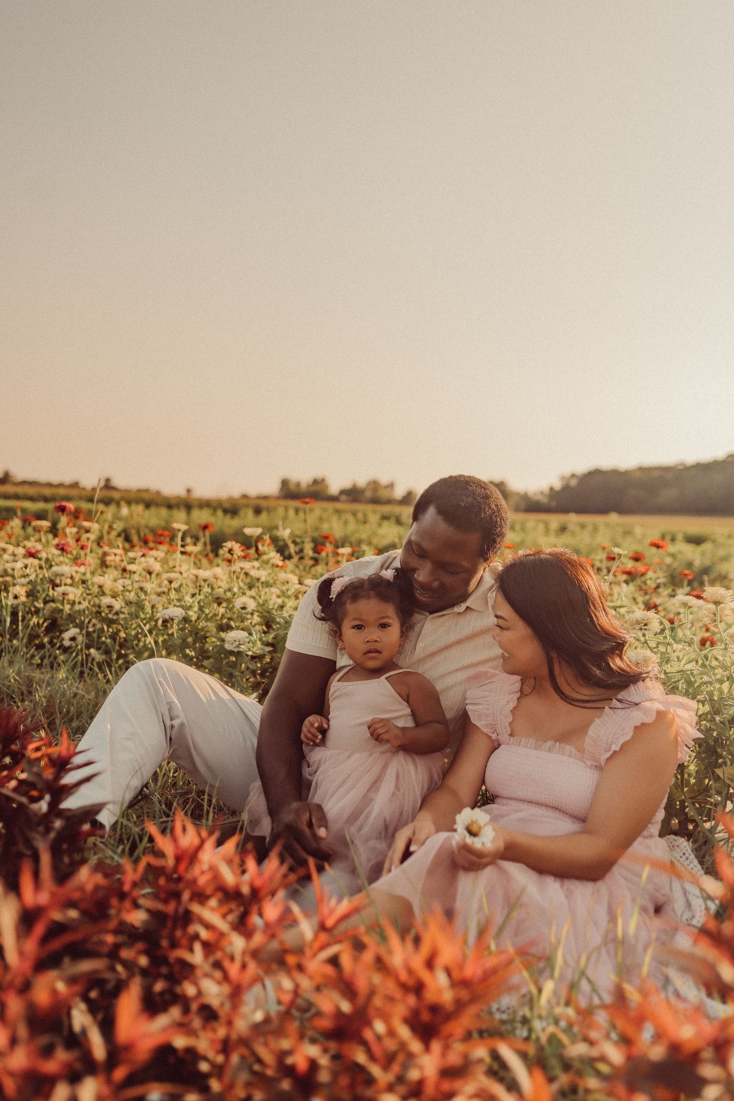 A family relaxes together in a field of vibrant orange flowers during golden hour.