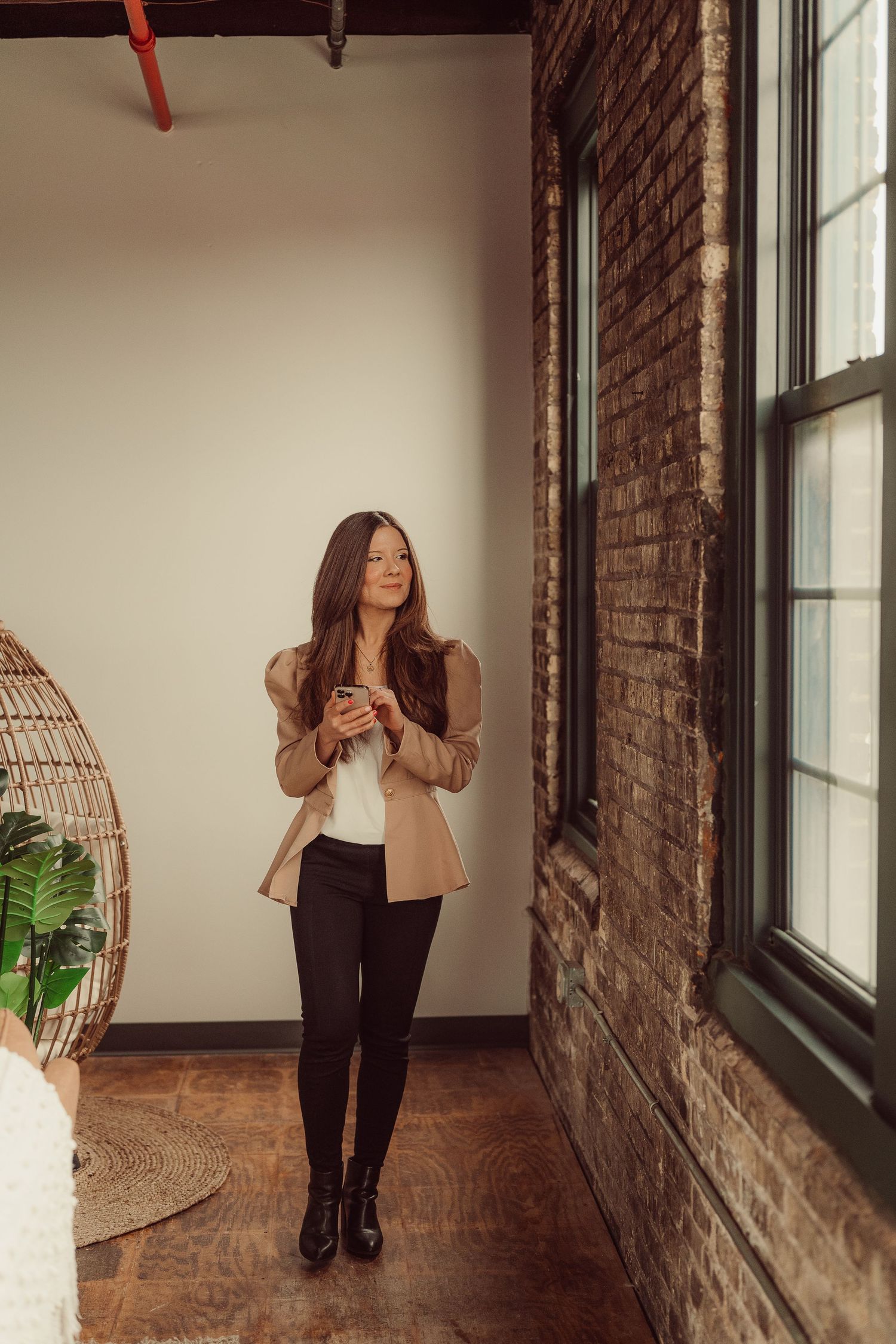 Professional portrait of a fresh style featuring beige blazer and black pants in an industrial loft setting.