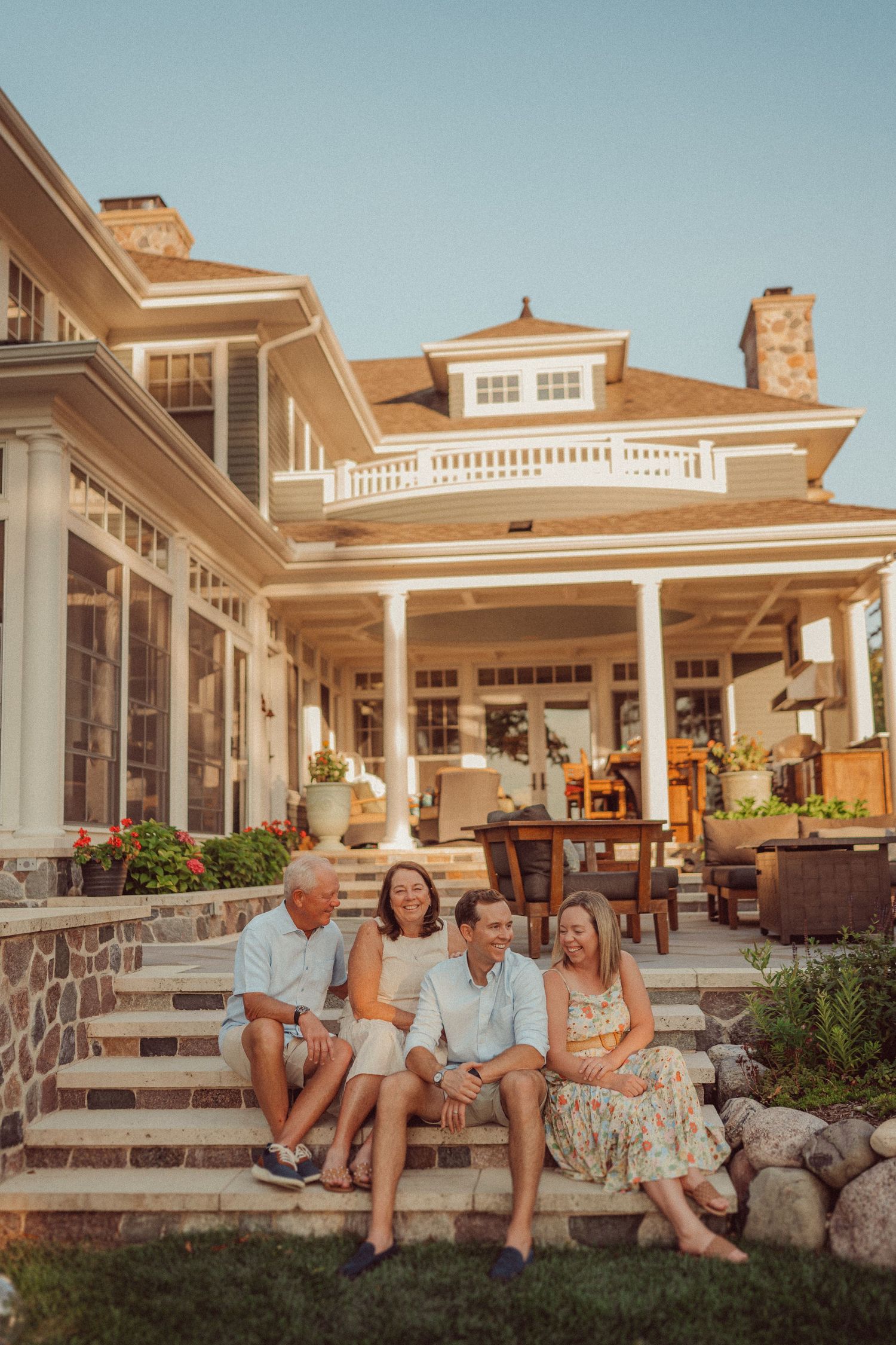 Family members sit on stone steps of an elegant coastal home during sunset.