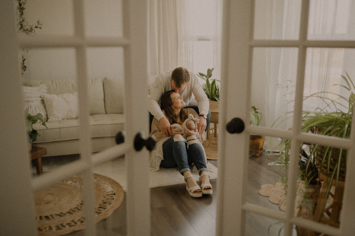 Cozy family moment viewed through French doors showing parent and child reading on white couch.