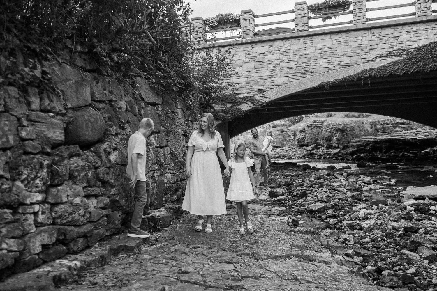 A family poses under a stone bridge archway in a black and white photograph.