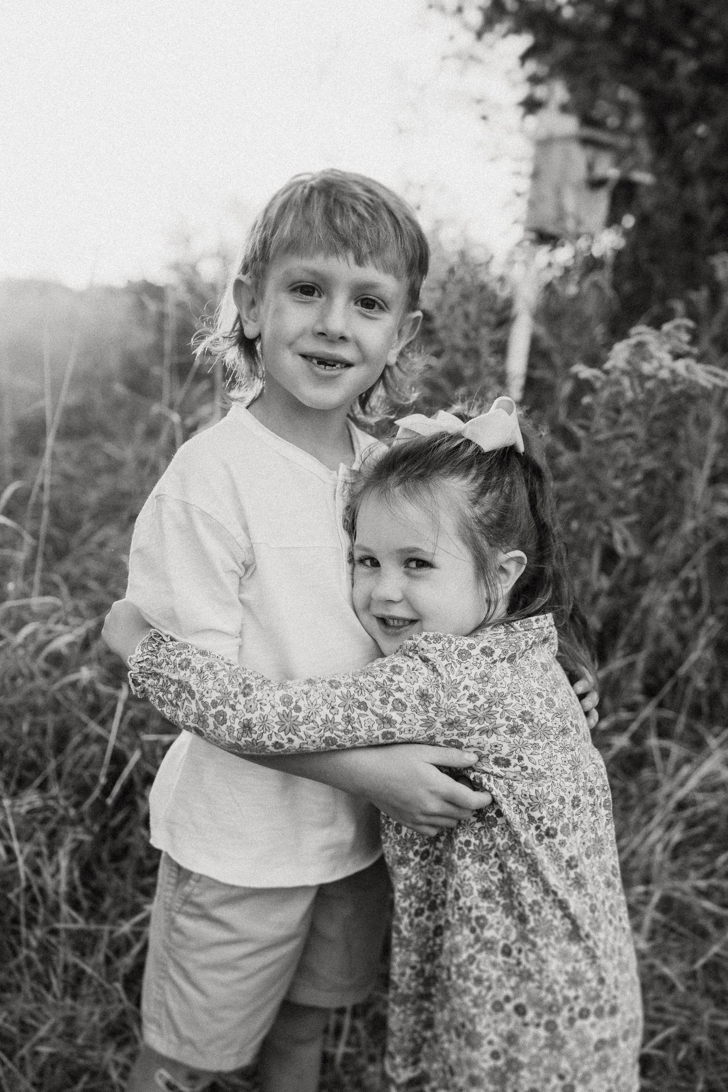Black and white portrait of two children hugging in a field.