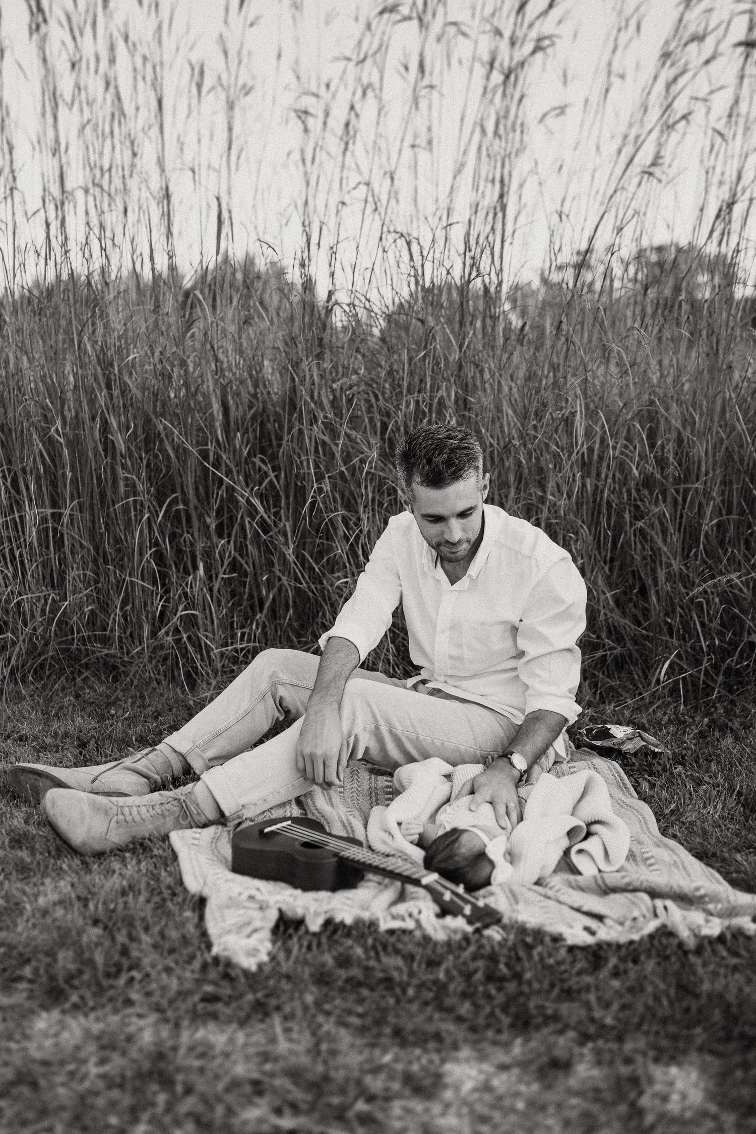 Black and white image of a parent and baby resting on a blanket surrounded by tall grass.