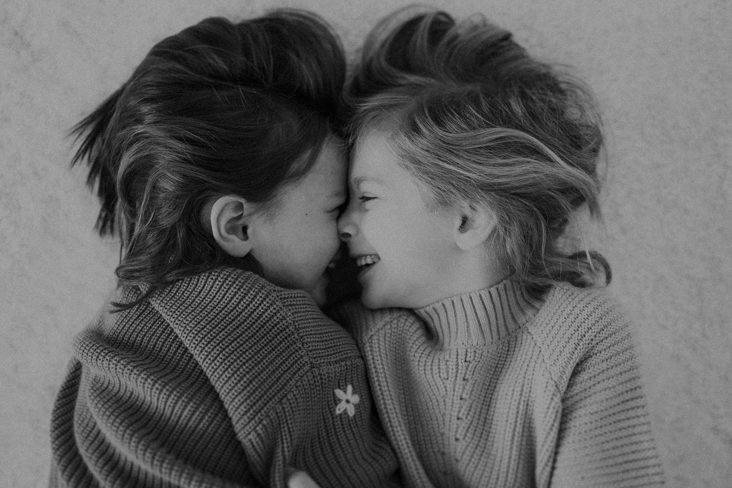 An intimate black and white portrait shows two people in sweaters touching foreheads.