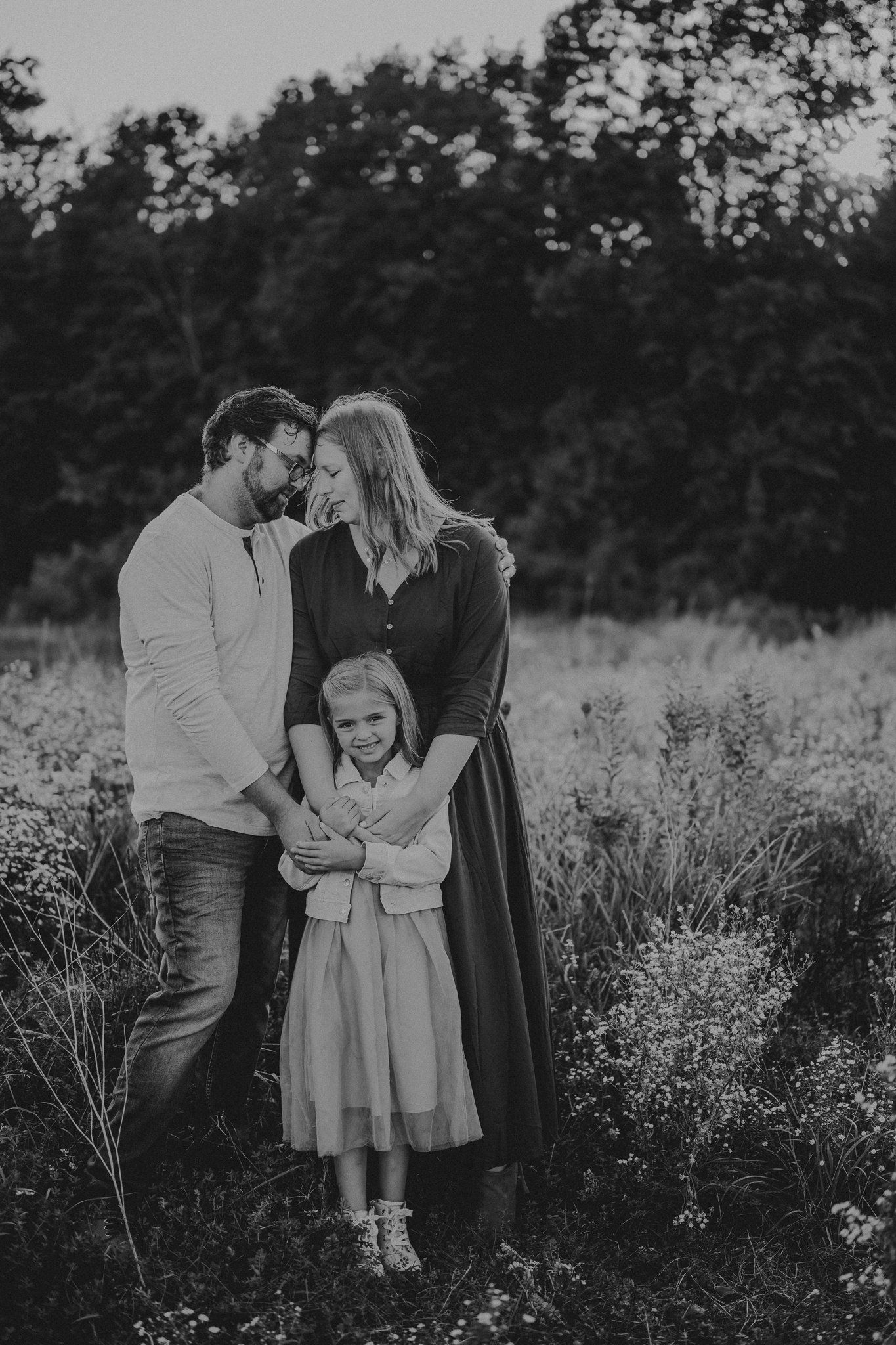 Black and white family portrait capturing an intimate moment in a wild meadow.