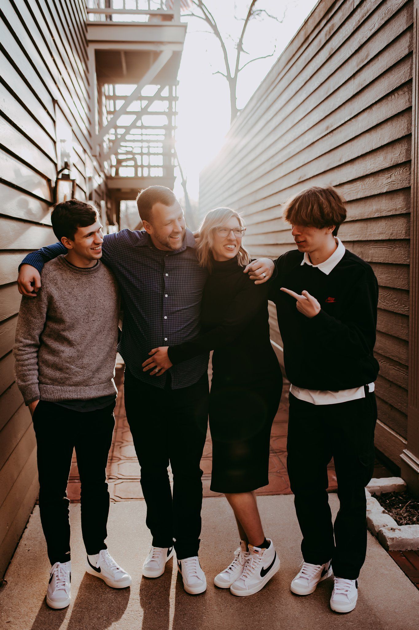 Group of friends in casual wear sharing candid moment in alley between wood-paneled buildings.