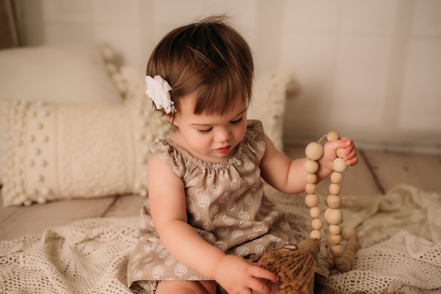 Baby playing with wooden bead garland on cream textured blanket in studio setting.